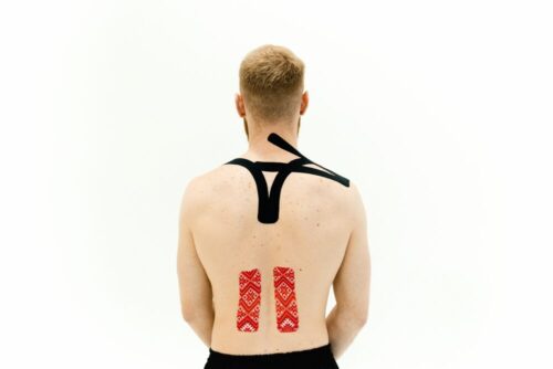 Man with kinesio tape on his back for muscle support and pain relief. Medical treatment with white background.