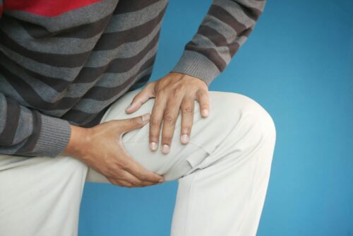 Close-up of a man's hands on his knee, showing pain or injury, on a blue background.