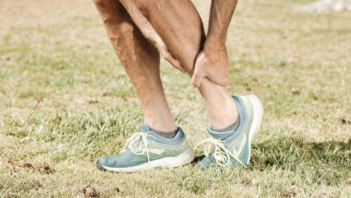Man holding his calf in pain, wearing teal sneakers on green grass.